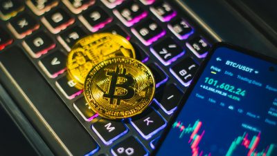 Close-up of gold Bitcoin coins on a backlit keyboard with trading app on smartphone.