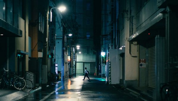 Nighttime city street with a lone pedestrian crossing, illuminated by streetlights.