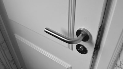 Close-up of a sleek steel door handle on a white door, showcasing modern interior design in monochrome.