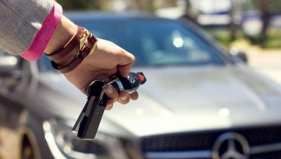 A close-up image of a hand holding car keys against the backdrop of a luxury car, outdoors.