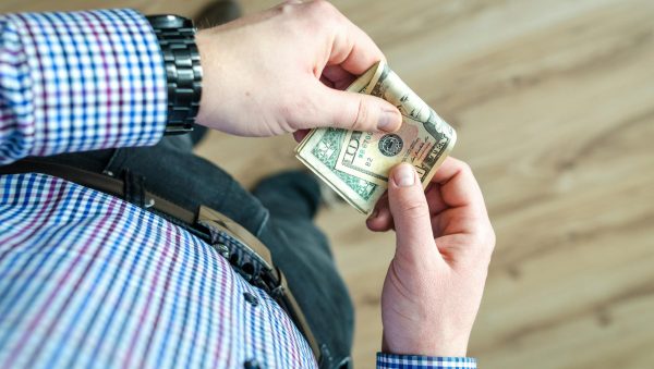Close-up view of a man in casual clothes holding US dollar bills in his hands.