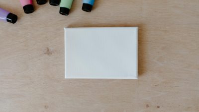 Top view of colorful paint tubes and blank canvas on a wooden surface.