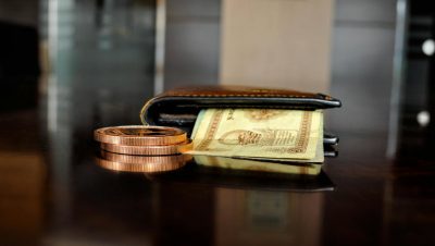 Arrangement of antique coins and banknotes beside a wallet, reflecting luxury finance.