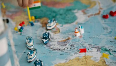 A detailed view of a world map with tiny model ships and flags indicating locations, highlighting global trade routes.