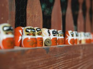 Colorful daruma dolls line up on a rustic wooden fence, symbolizing Japanese culture and tradition.